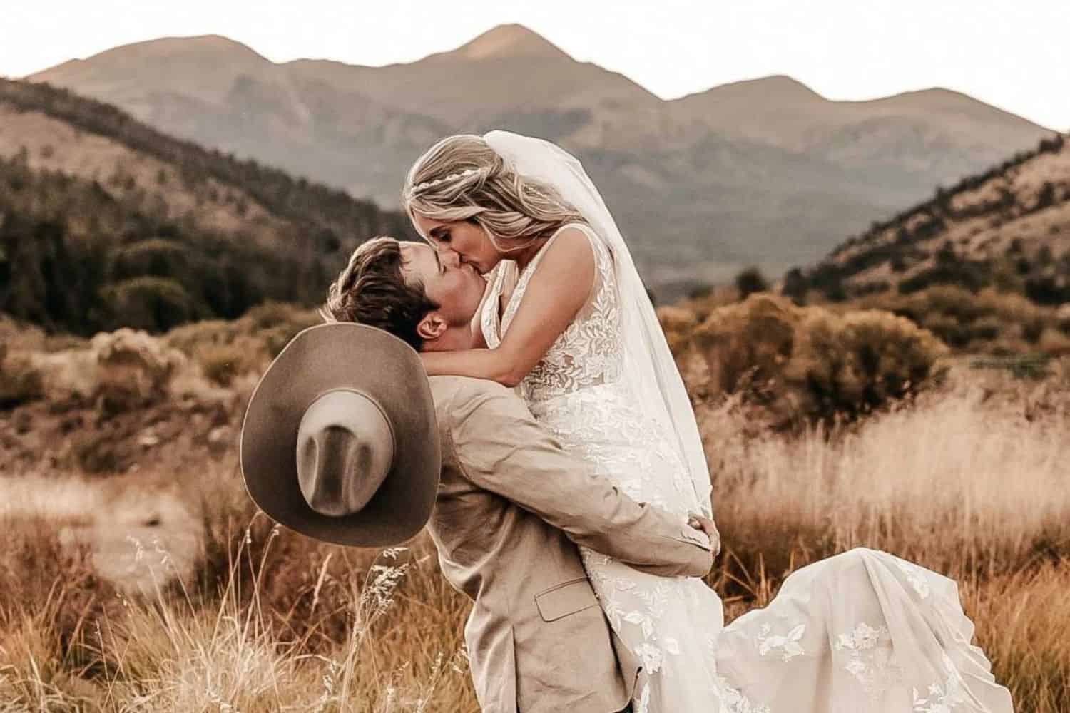 Elegant wedding scene with a bride and groom sharing a kiss in nature.